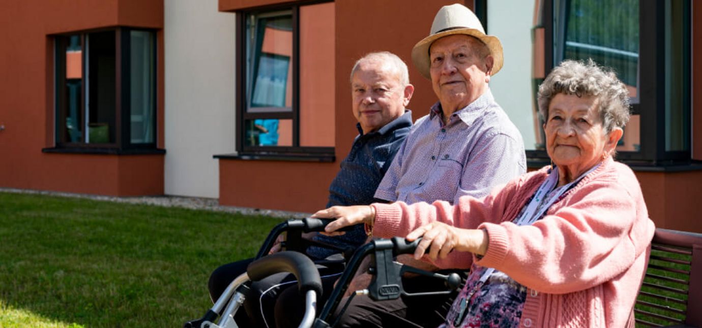 drei Senioren sitzen bei Sonnenschein im Vorgarten auf einer Bank
