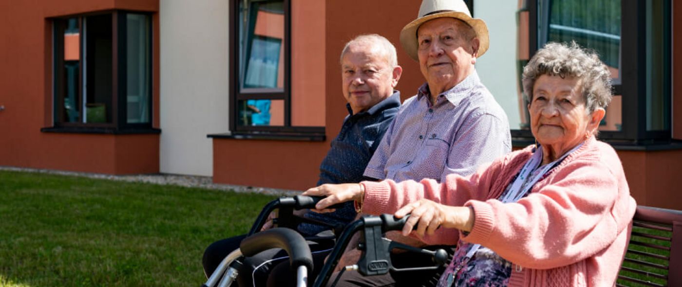 drei Senioren sitzen bei Sonnenschein im Vorgarten auf einer Bank
