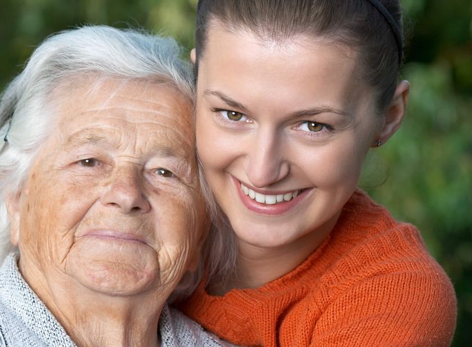 Junge Frau legt älterer Frau die Hände auf die Schulter