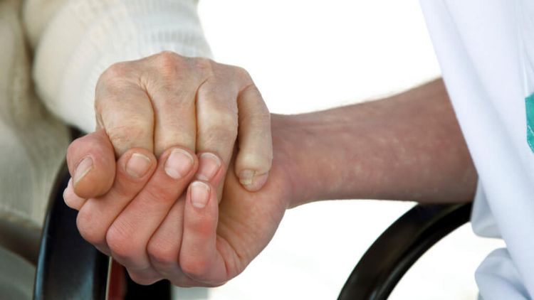 Pflegerin hält Hand eines älteren Bewohners