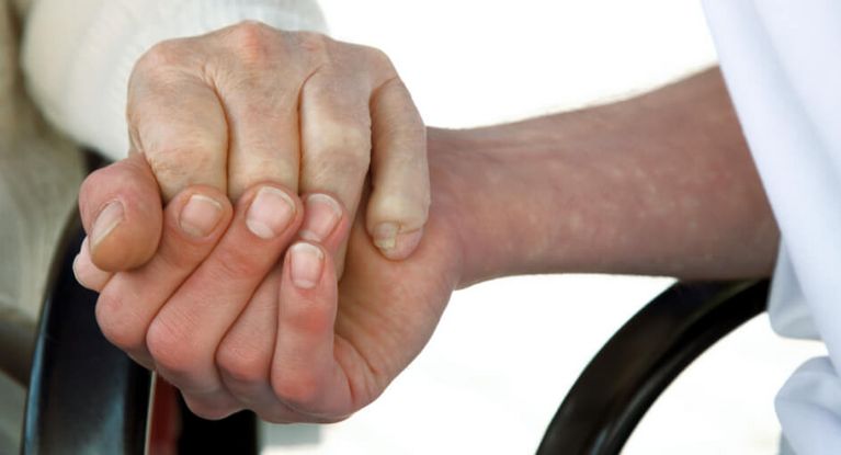 Pflegerin hält Hand eines älteren Bewohners