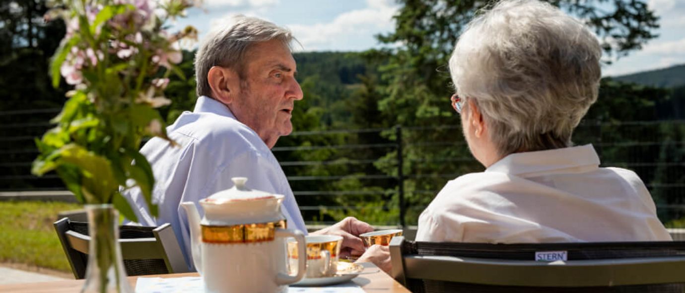 Seniorenpaar sitzt draußen am Tisch beim Kaffeetrinken