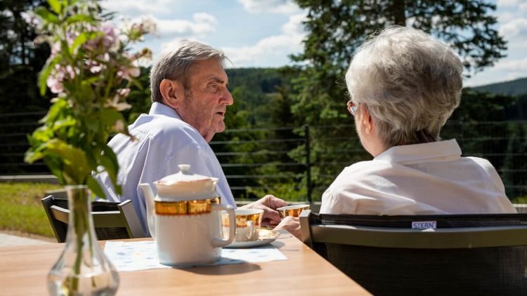Seniorenpaar sitzt draußen am Tisch beim Kaffeetrinken