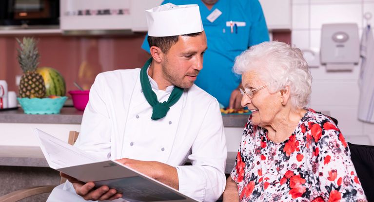 Koch und Seniorin studieren gemeinsam die Speisekarte